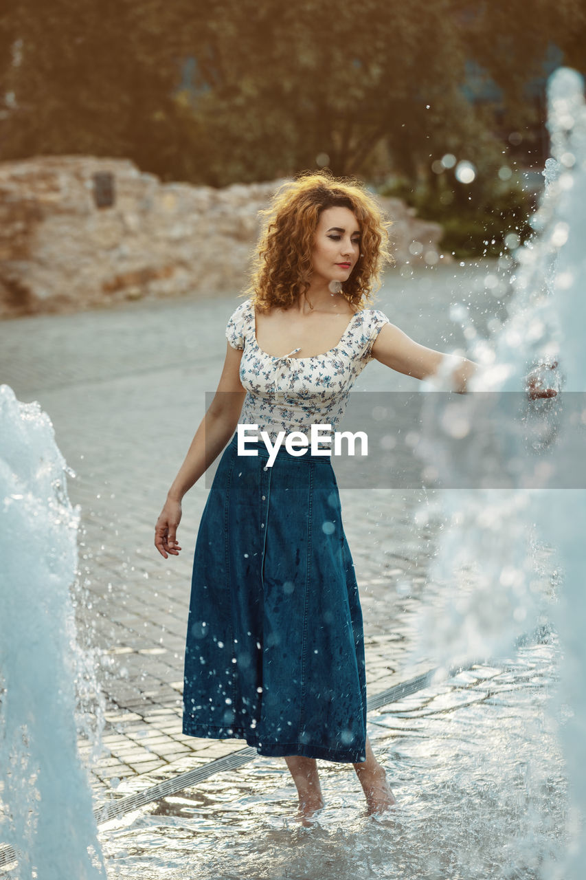 Youn moroccan woman, with curly brown hair, wearing a jean skirt, playing with water at a fountain