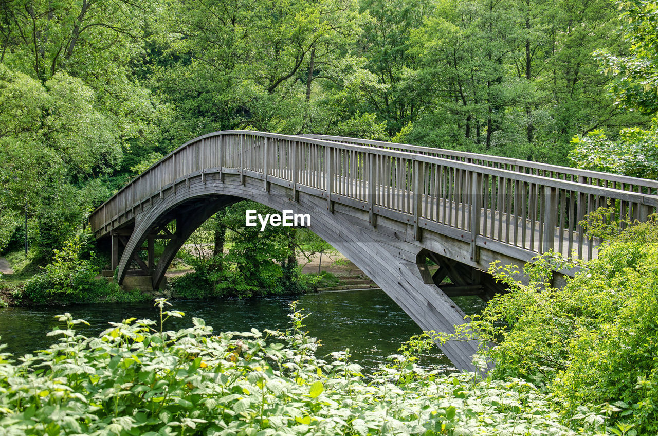 Wooden arch bridge for pedestrians across the river rur in an overwhelmingly green environment