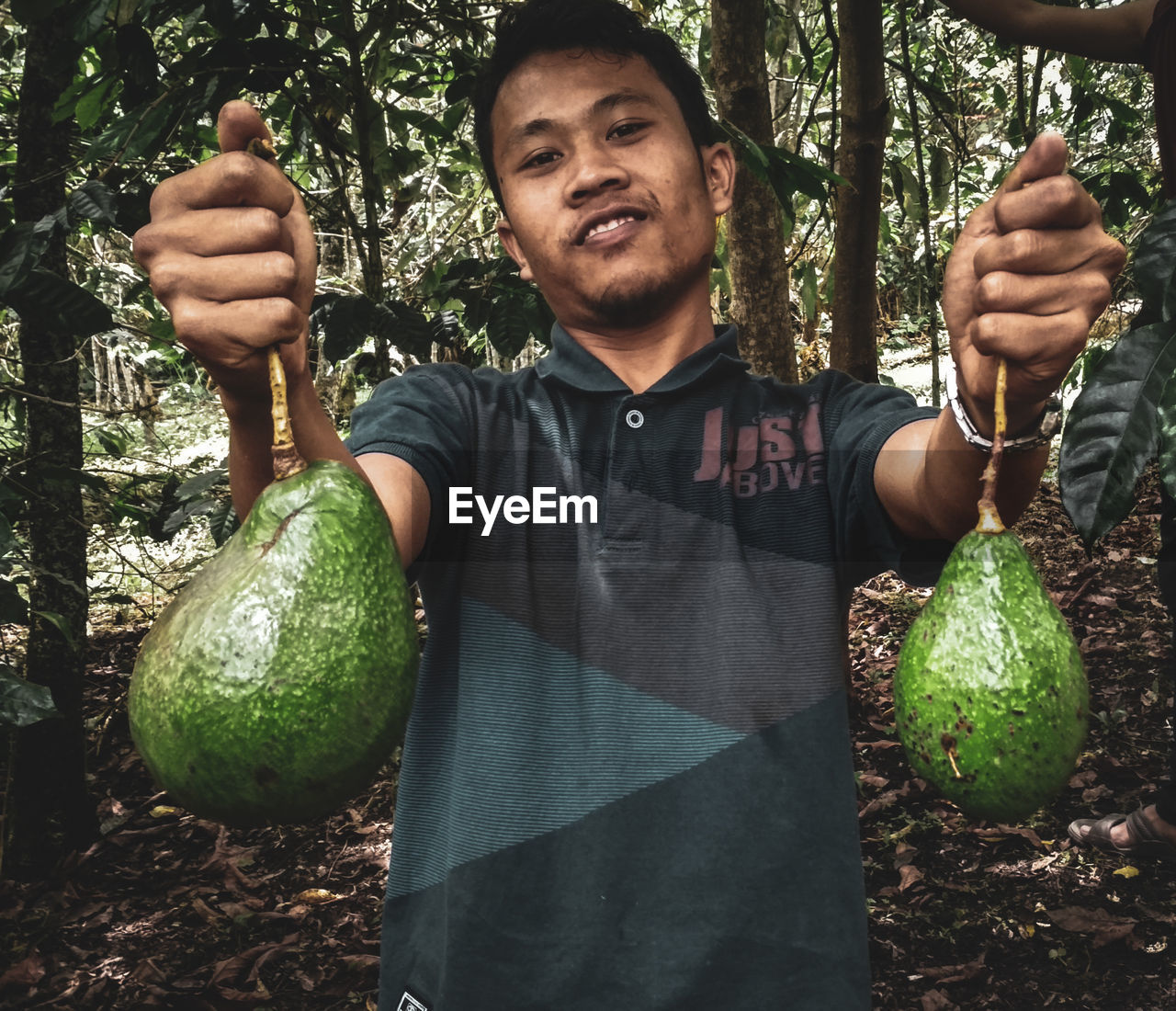 Portrait of man holding fruits while standing in forest