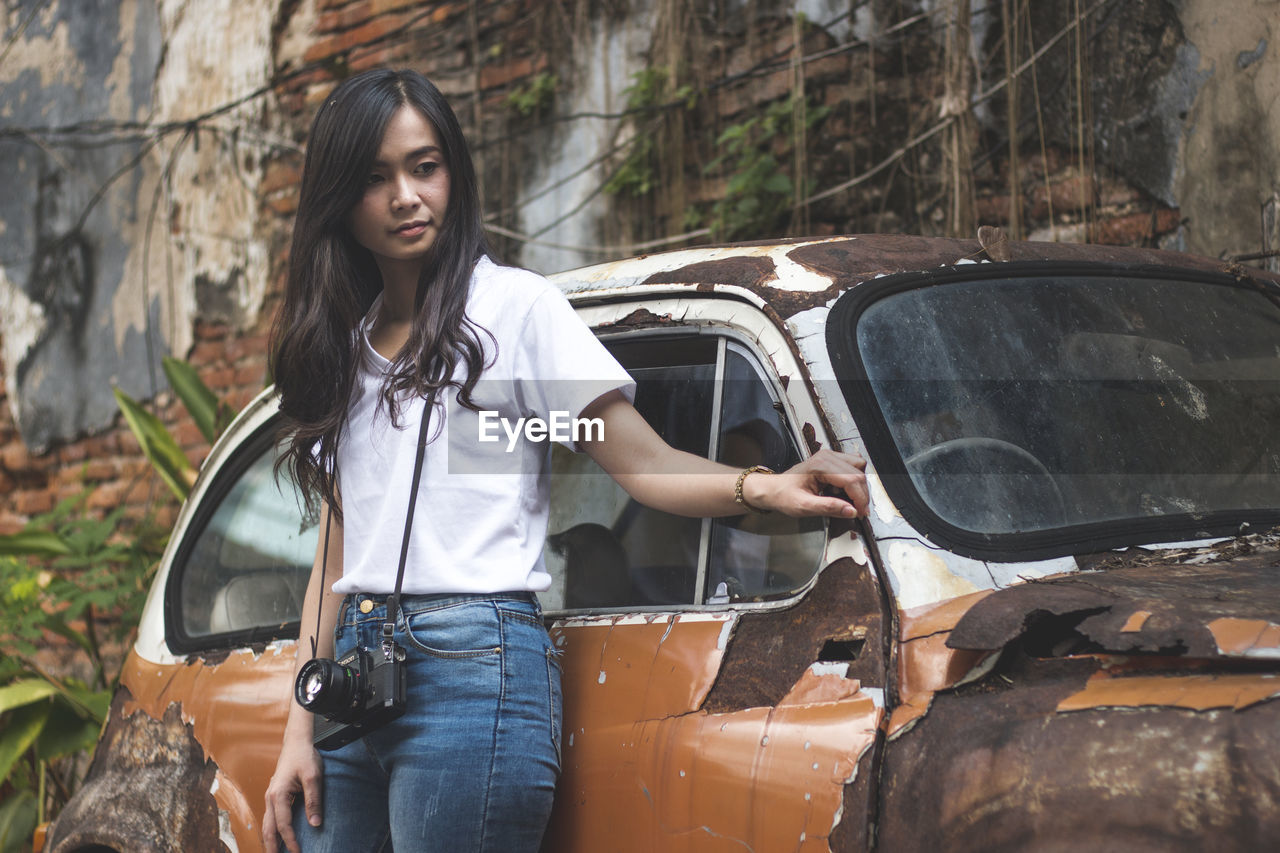 Young woman standing by abandoned car