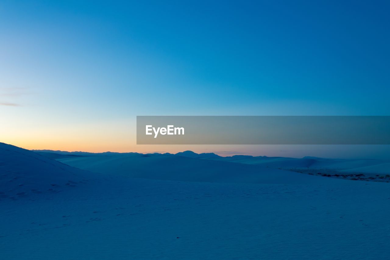 Scenic view of snowcapped mountains against clear blue sky during sunset