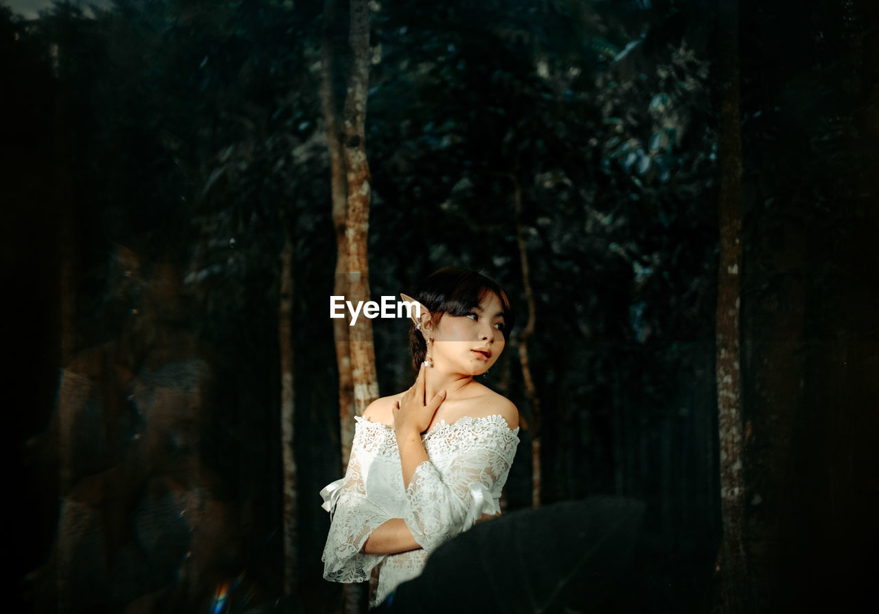 Woman looking away while standing against tree trunk