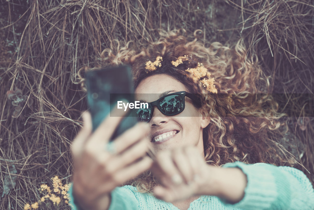 High angle view of woman taking selfie with smart phone while lying on land