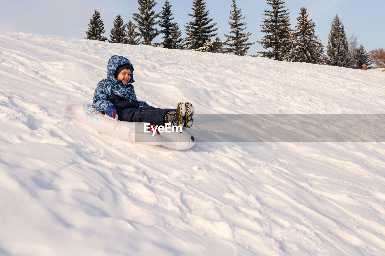 Young boy sliding down a snowy hill on a toboggan