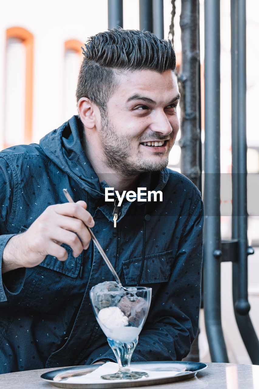 Smiling young man eating ice cream while sitting at restaurant