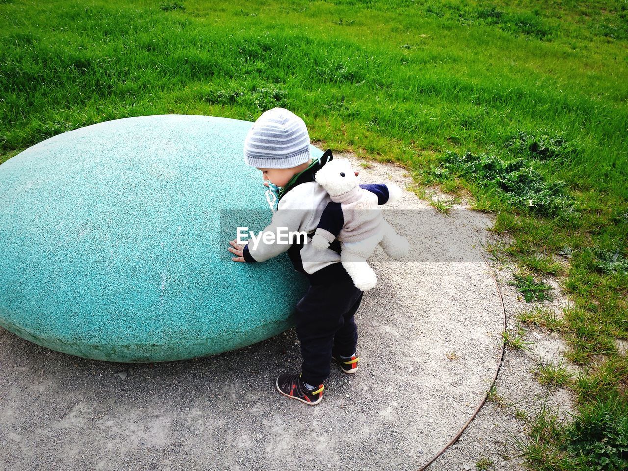 High angle view of boy standing by blue stone against grassy field at park