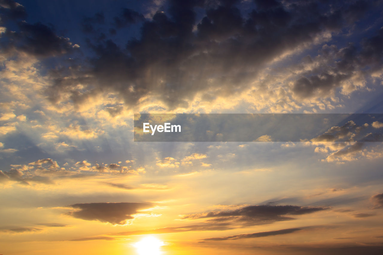 Low angle view of sunlight streaming through clouds during sunset