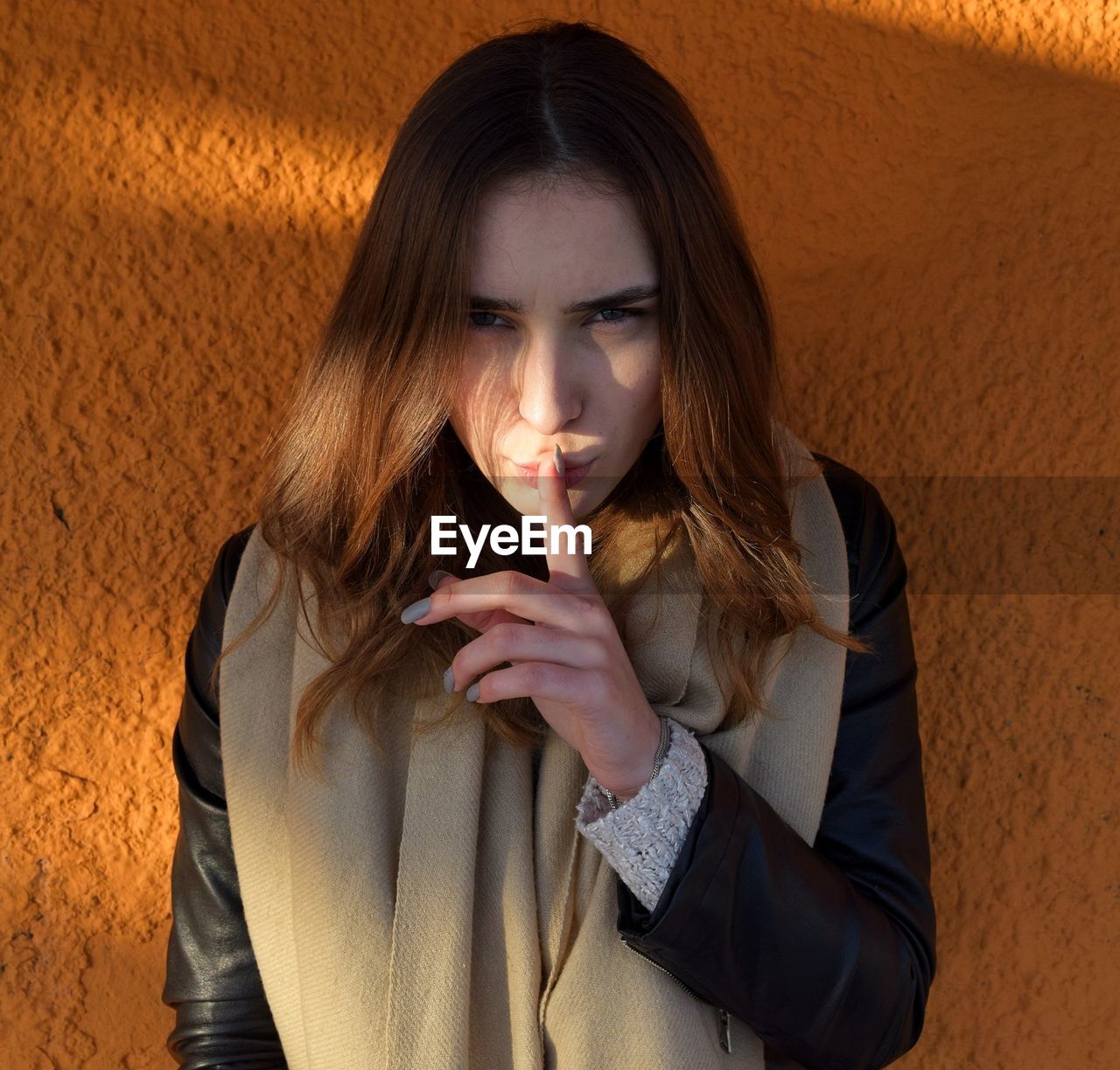 Close-up portrait of young woman gesturing against wall