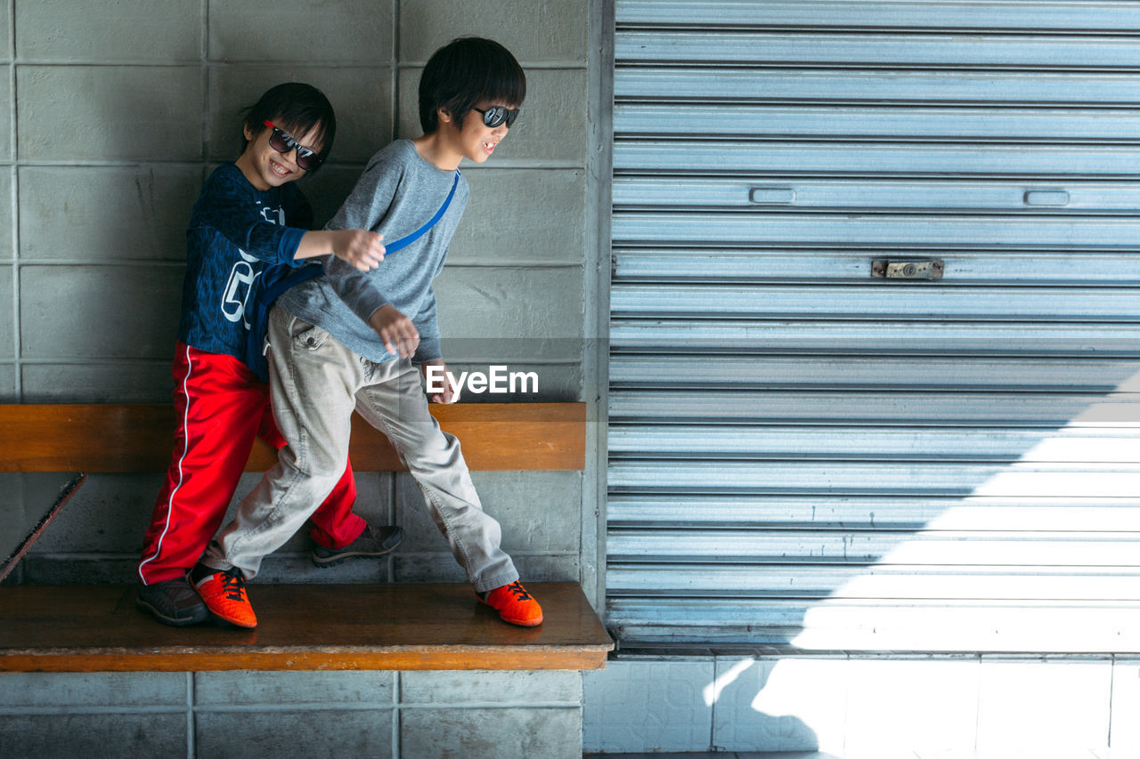 Siblings playing on bench against wall