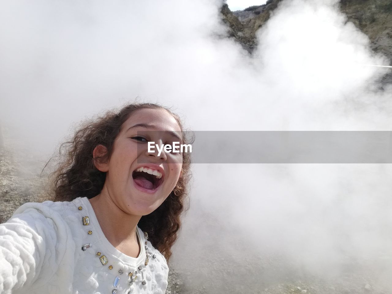 Portrait of cheerful girl standing against smoke during sunny day