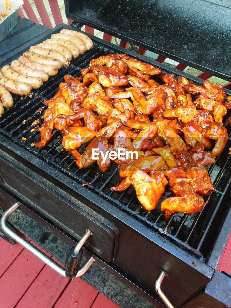 High angle view of chicken wings and sausages on barbeque