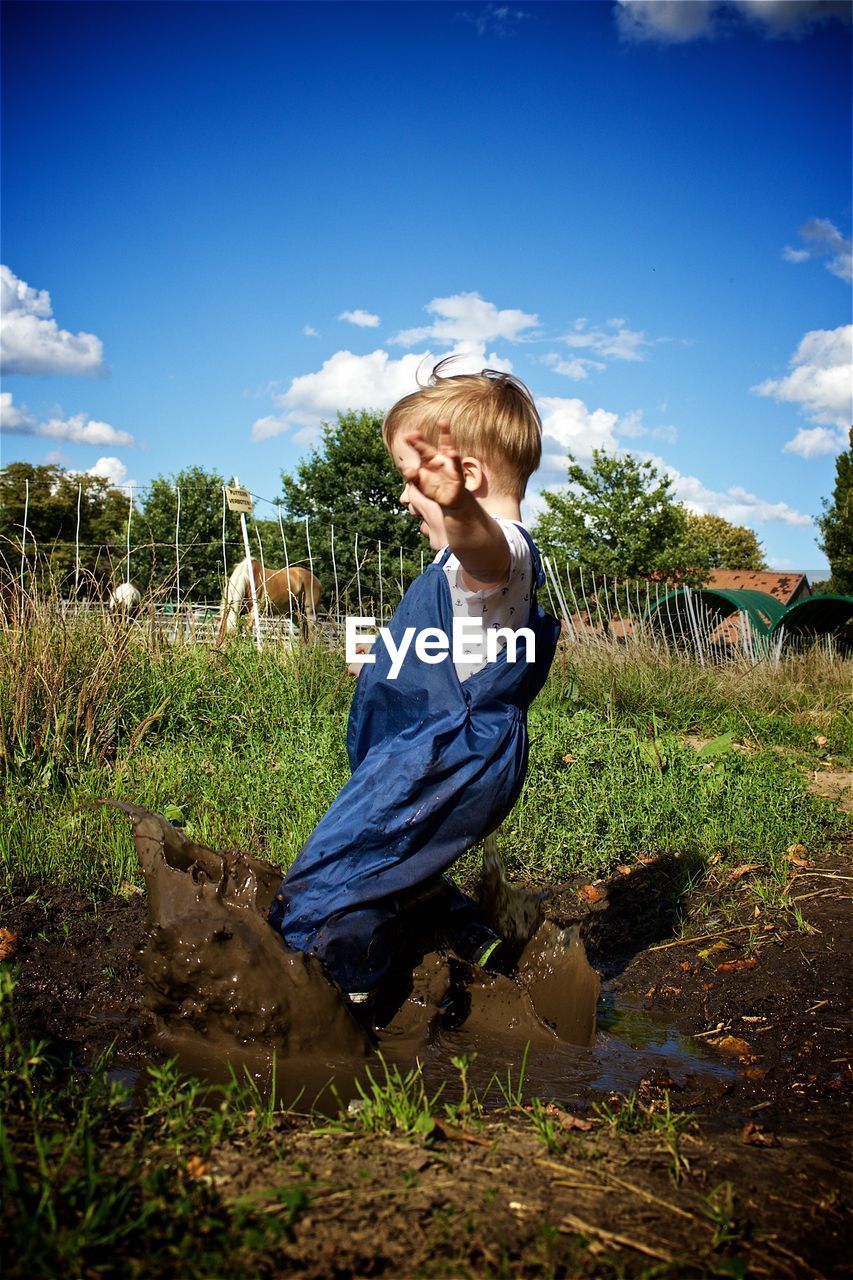 Full length of boy splashing mud on field against sky