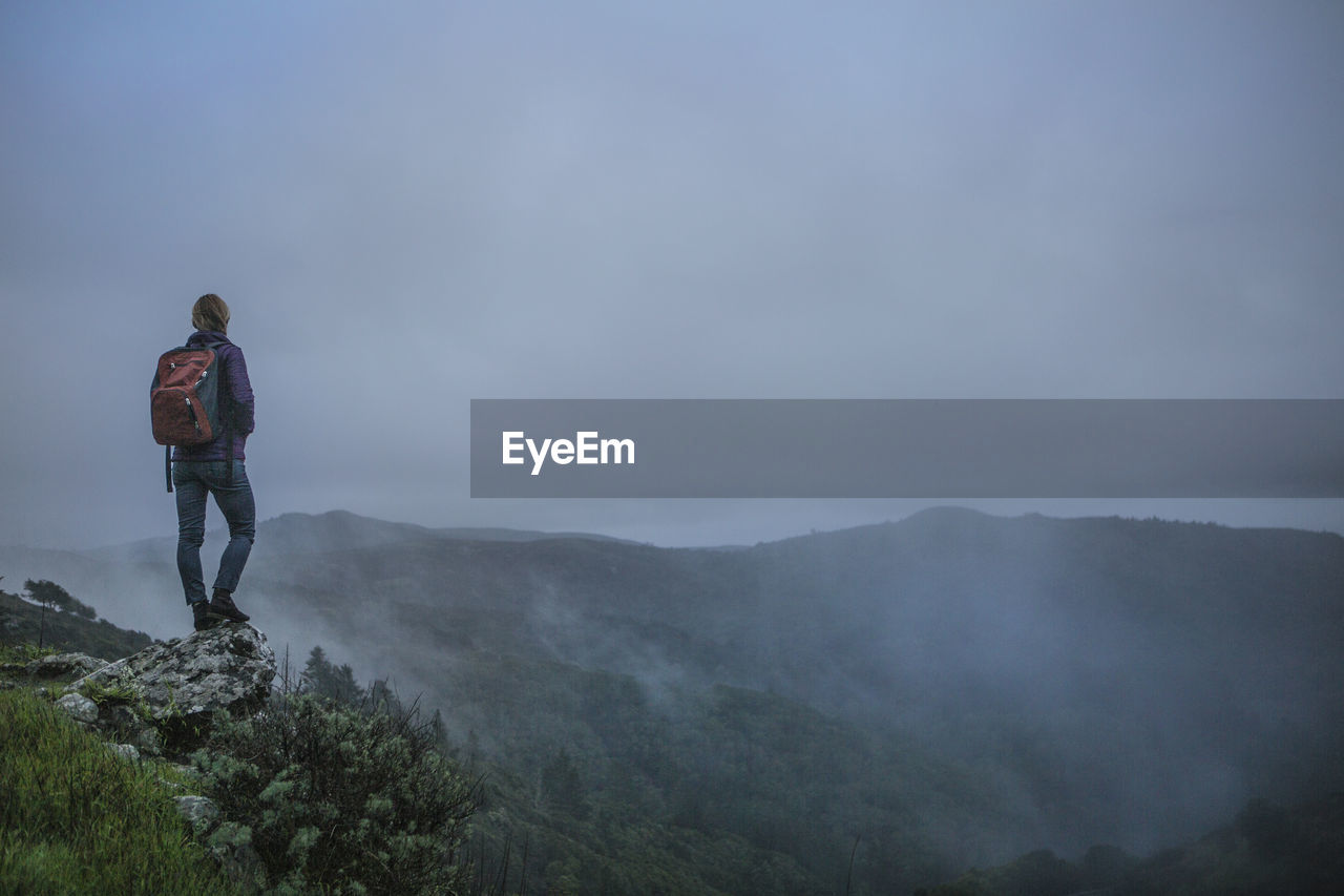 Rear view of man standing on mountain against cloudy sky