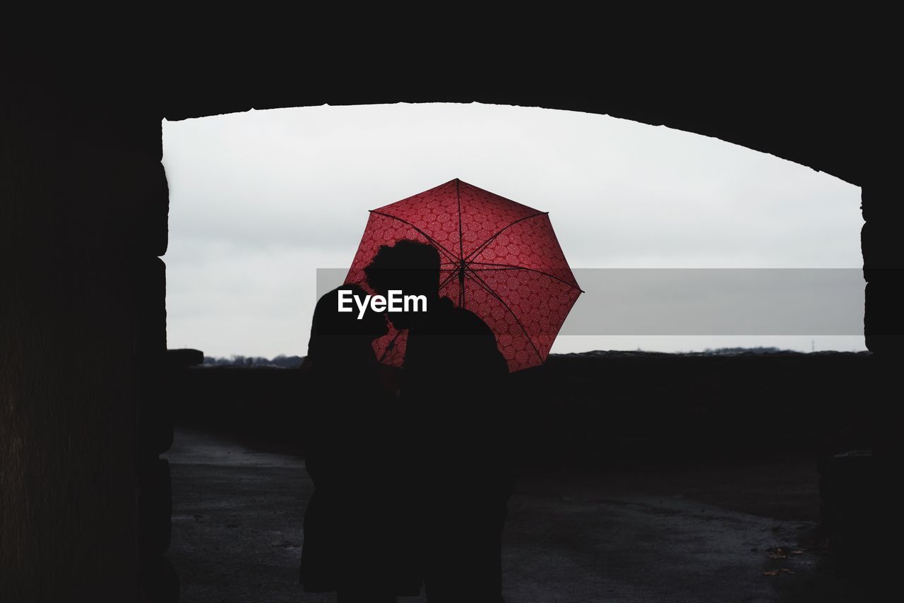 Silhouette of couple standing with umbrella kissing at archway