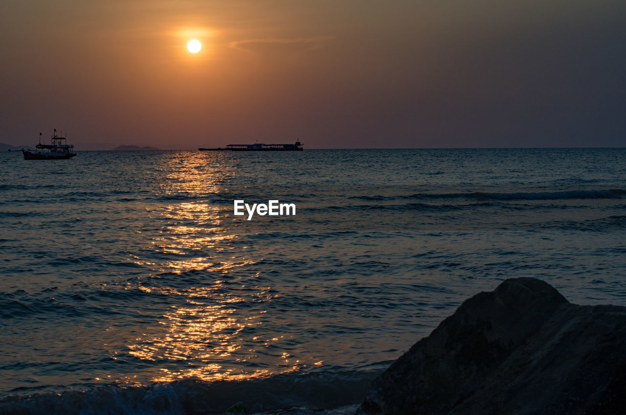 Silhouette boats in sea against orange sky during sunset