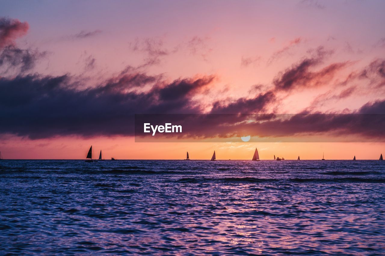 Silhouette sailboat sailing on sea against dramatic sky during sunset