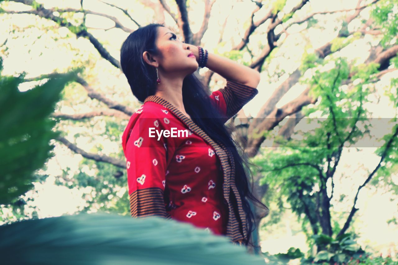 WOMAN LOOKING AWAY WHILE STANDING AGAINST TREE