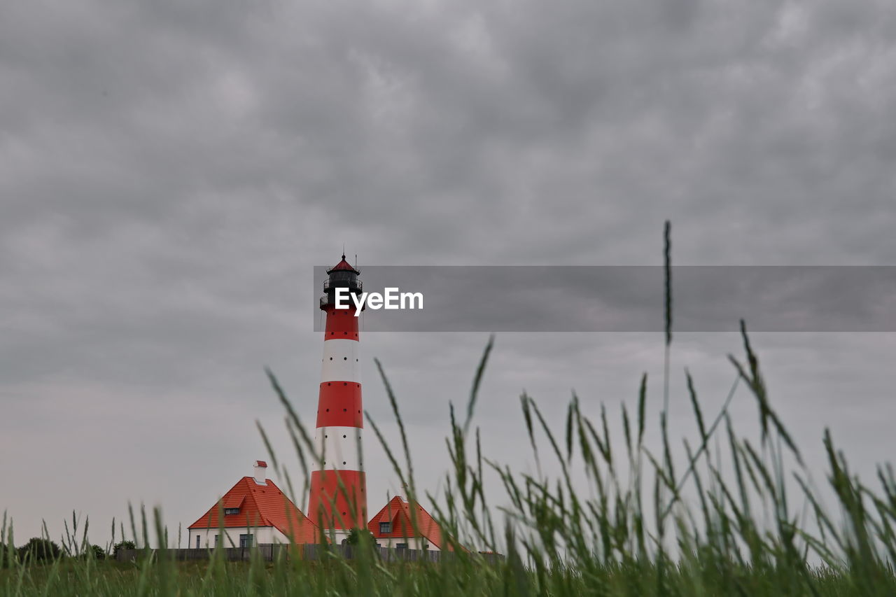 Lighthouse on field by building against sky