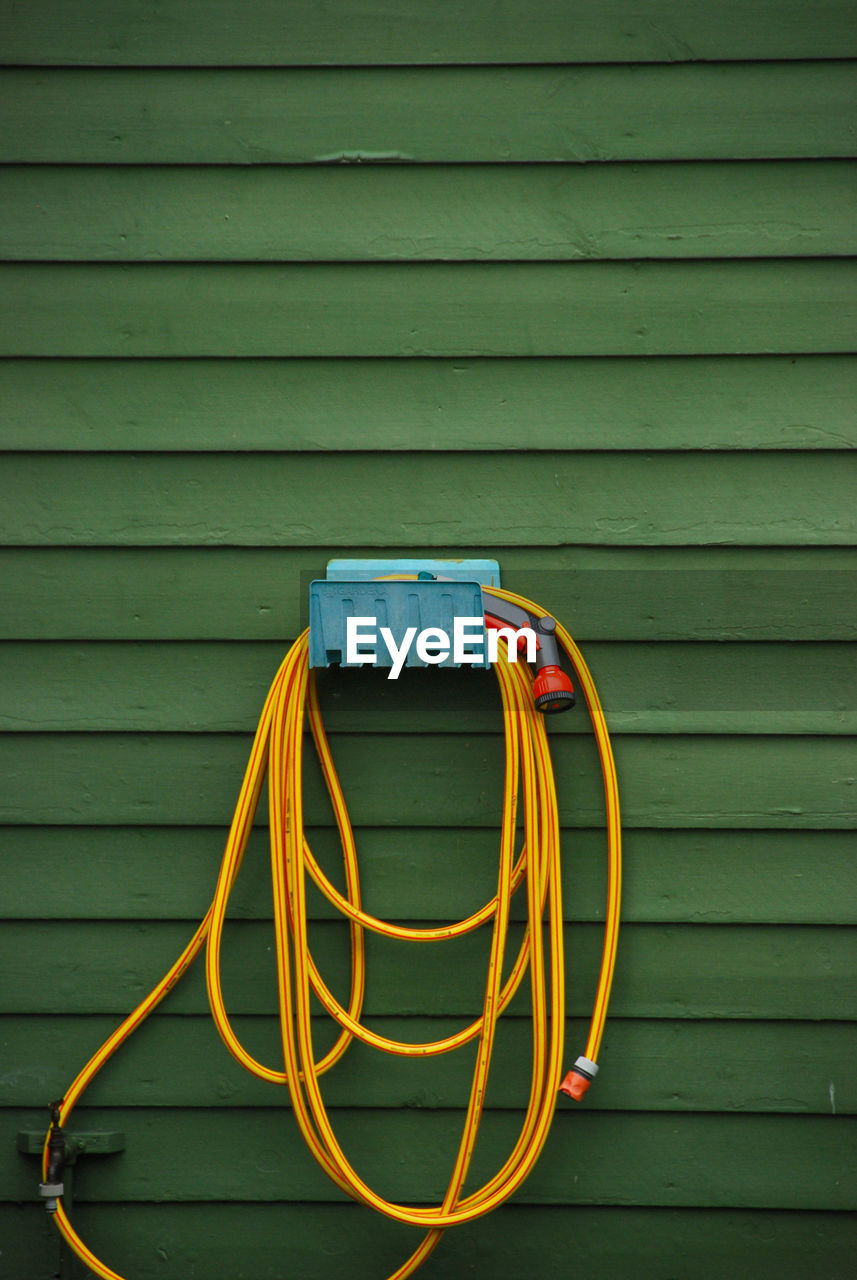 Garden hose hanging on green wall at yard