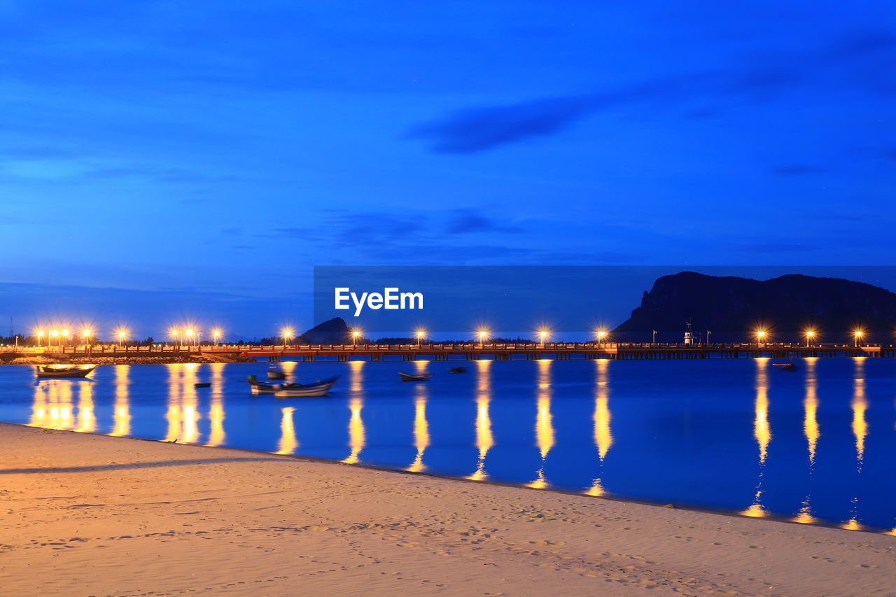 Illuminated bridge over sea against sky at night