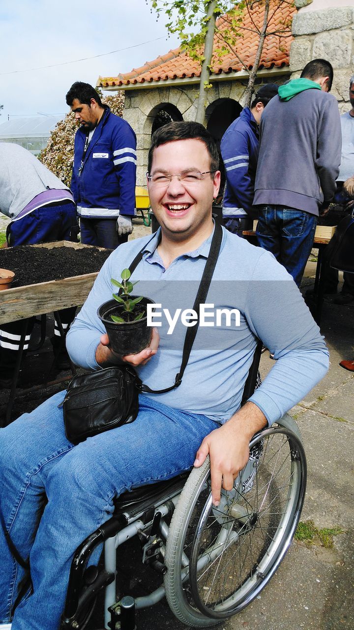 Portrait of smiling young man with potted plant sitting on wheelchair