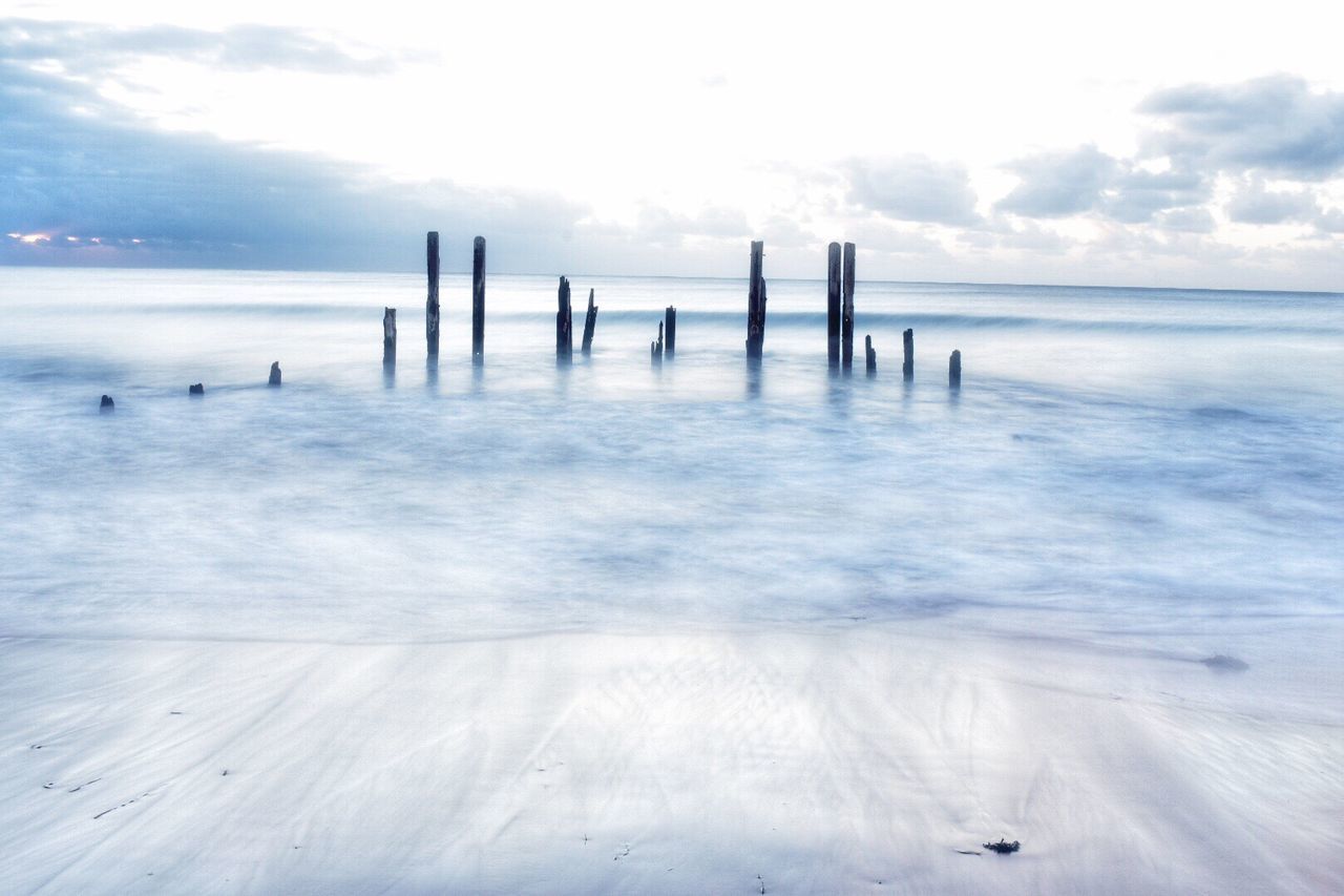 Wooden posts in sea against sky