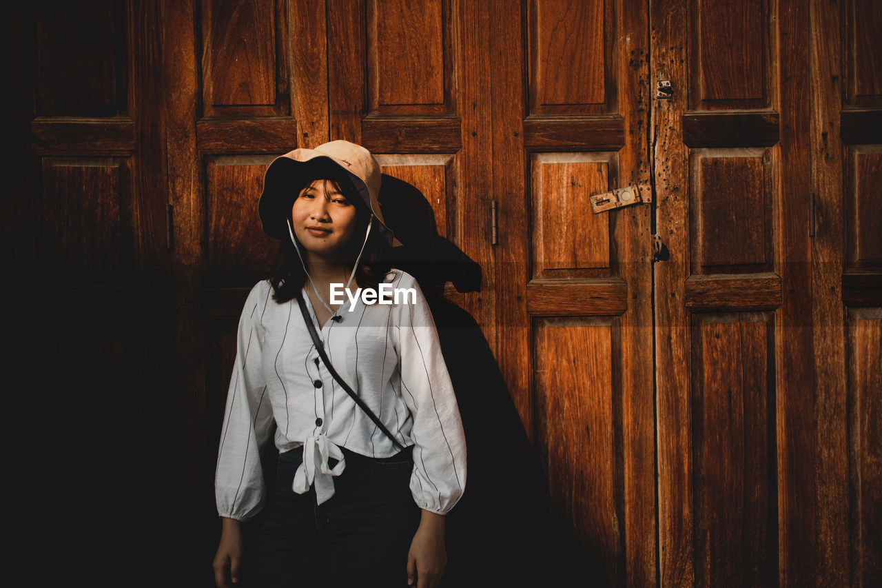 Young woman looking away while standing on wooden door