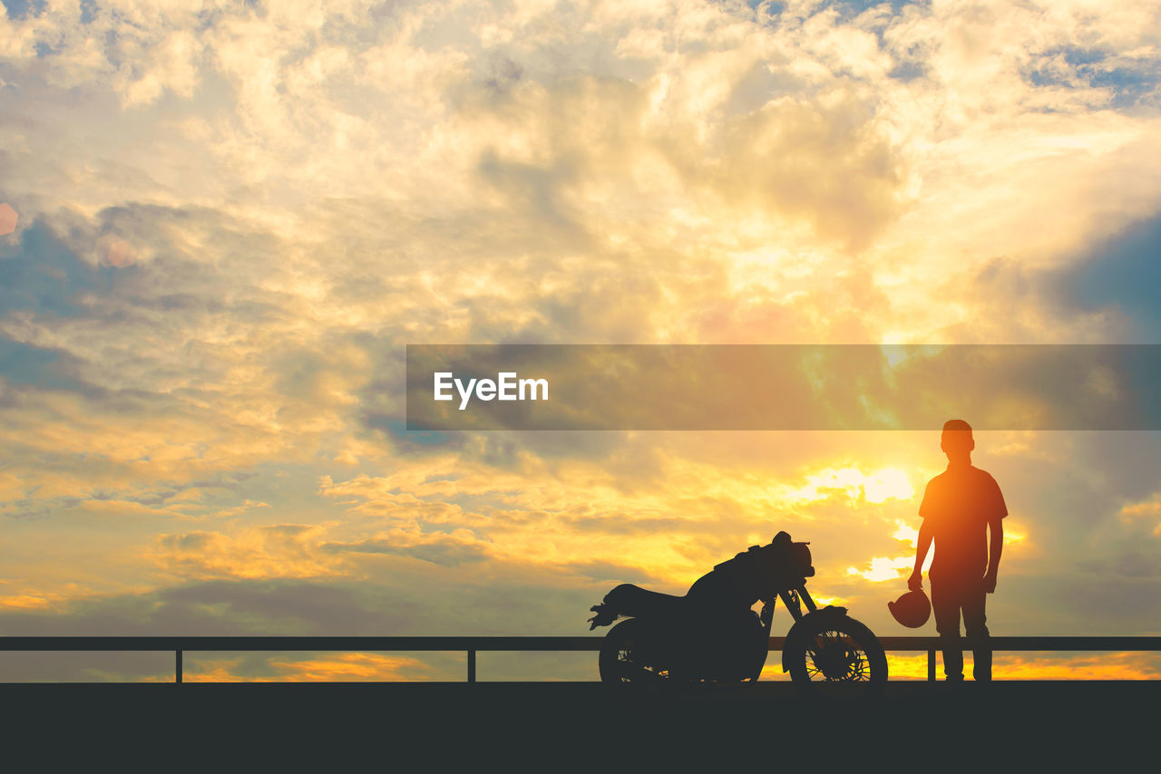 Silhouette man standing with motorcycle against cloudy sky during sunset