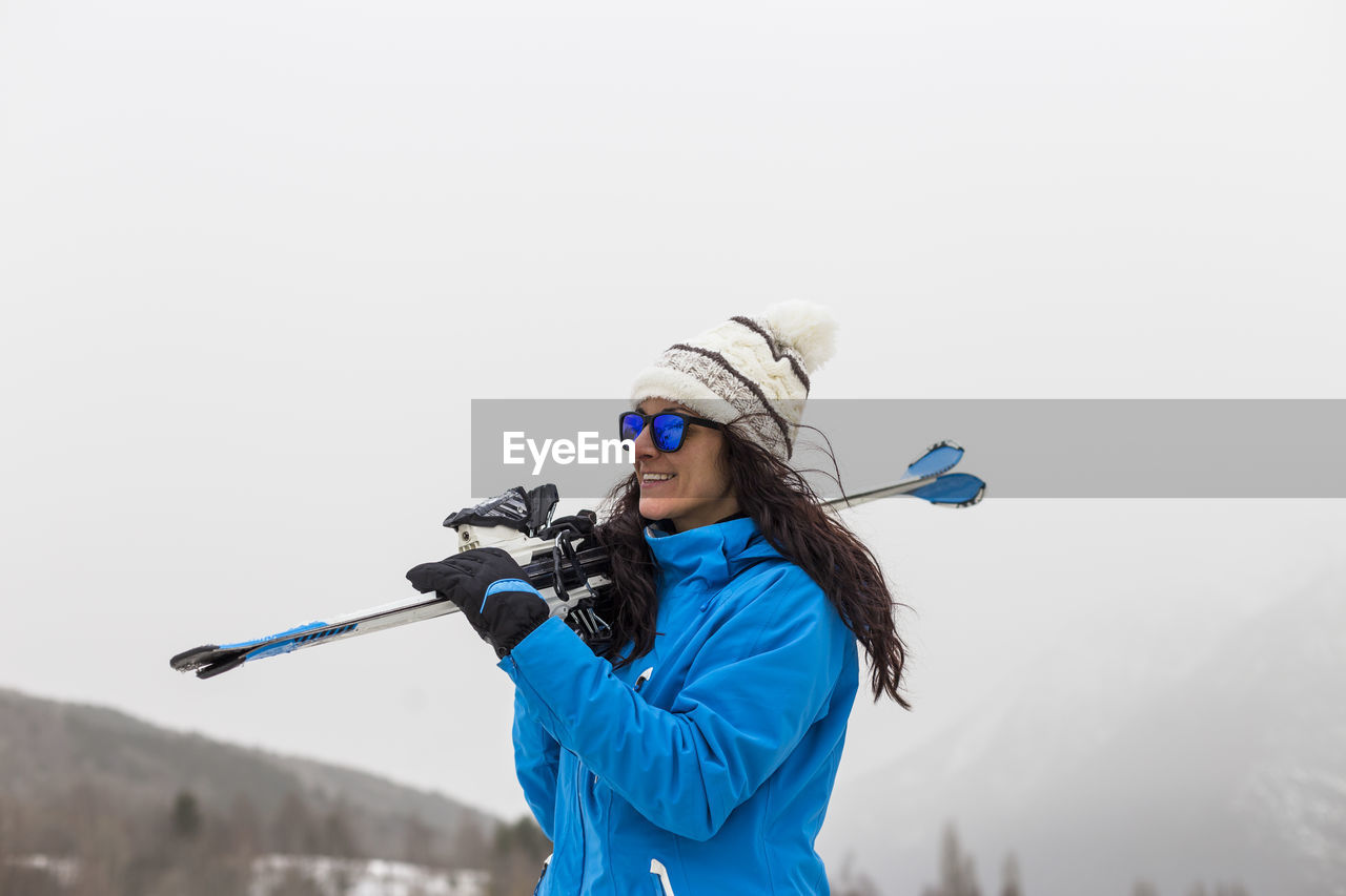 Smiling woman standing with snowboard against fog covered mountains during winter