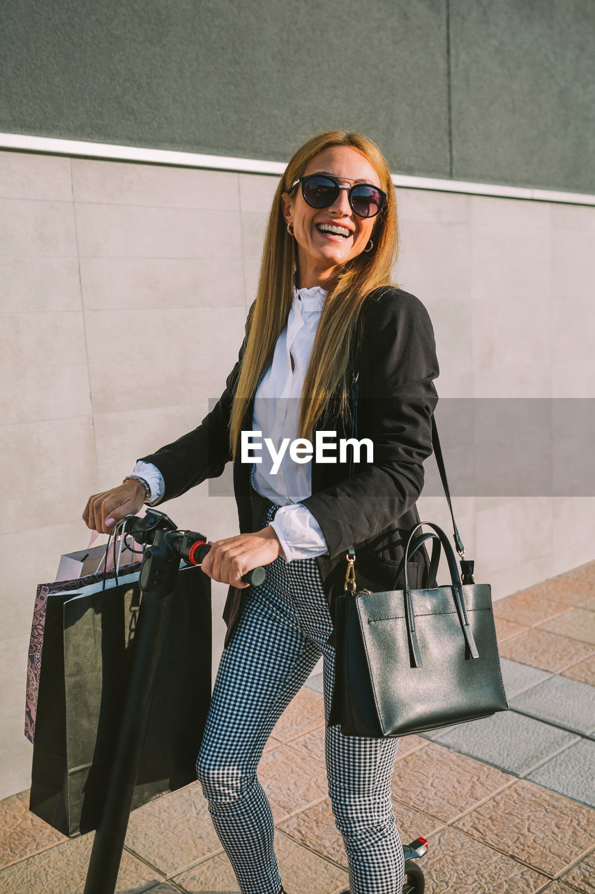 Smiling businesswoman riding electric push scooter on sidewalk