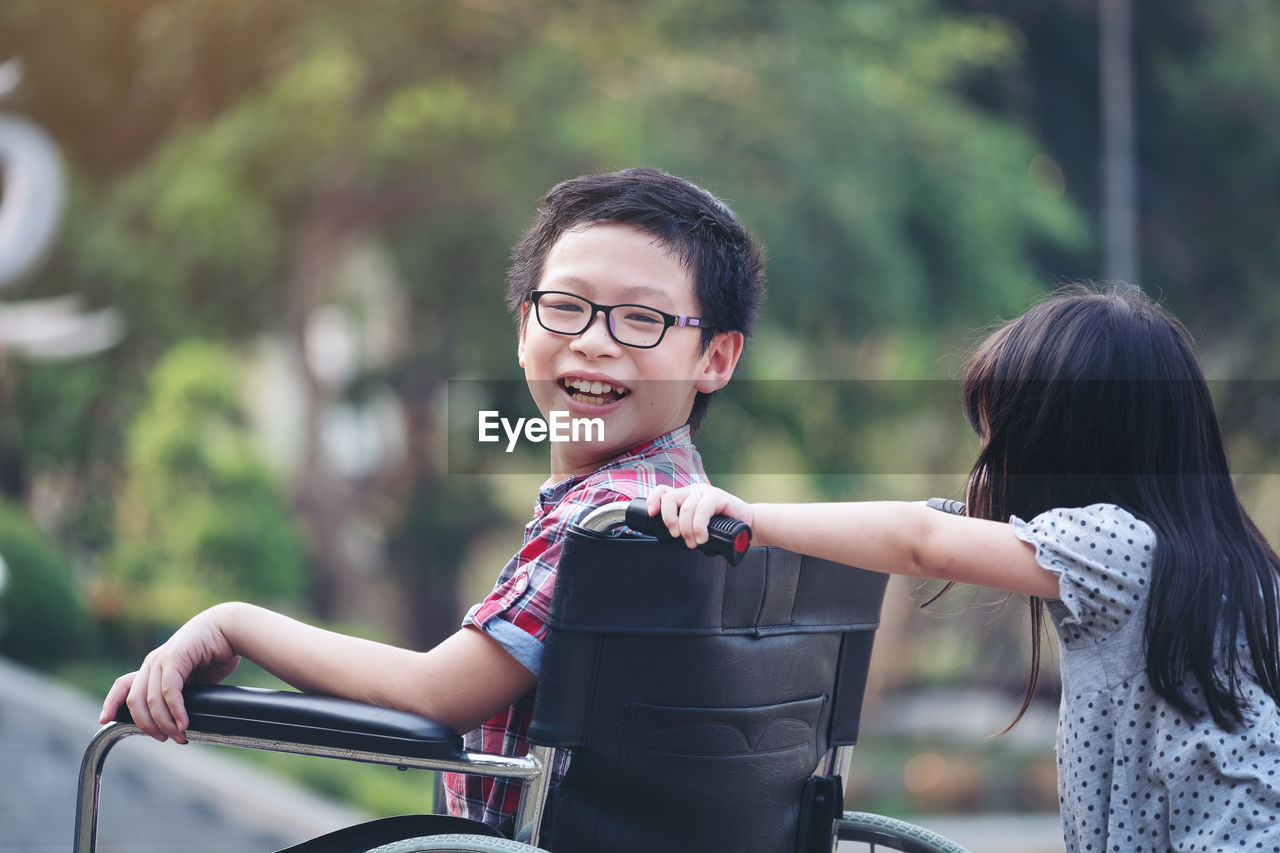 Portrait of happy boy sitting on wheelchair with sister