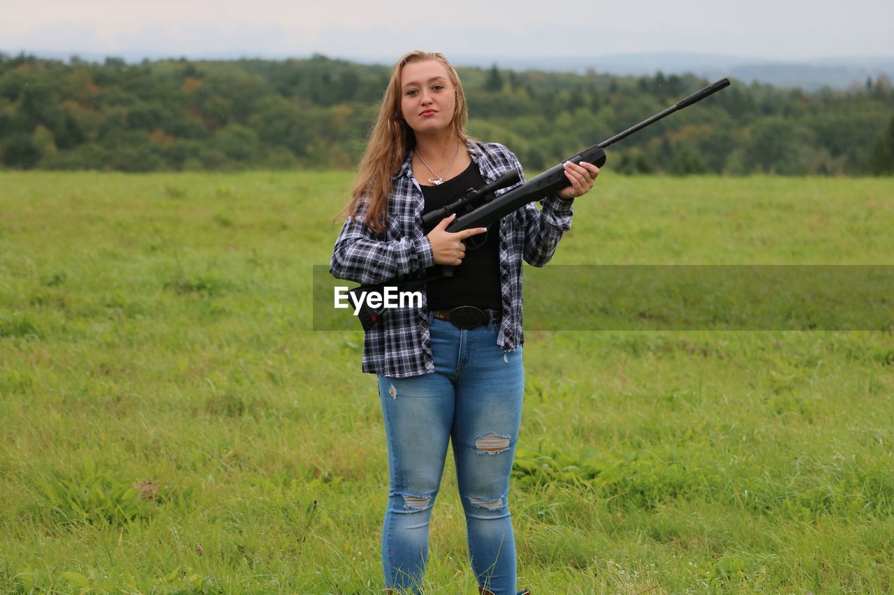 Portrait of teenage girl holding rifle while standing on field