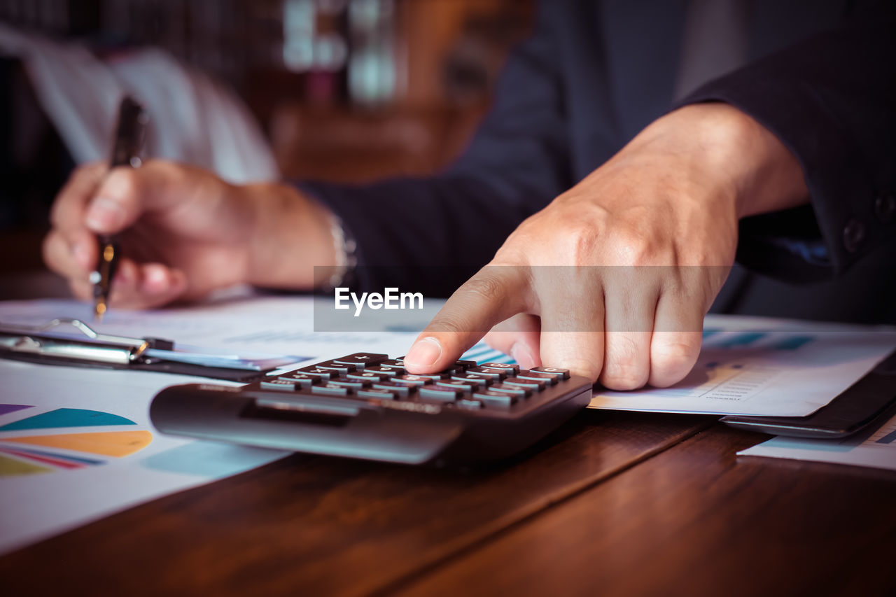 Midsection of businessman calculating on table