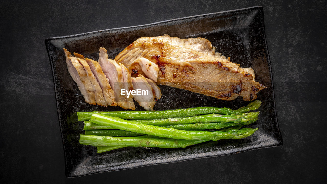 Fried pork with asparagus and pepper in black ceramic plate on dark tone background, top view