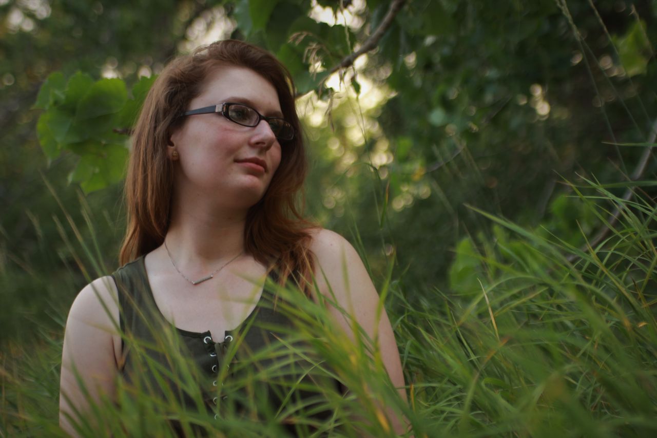 Thoughtful young woman wearing eyeglasses while looking away by grass