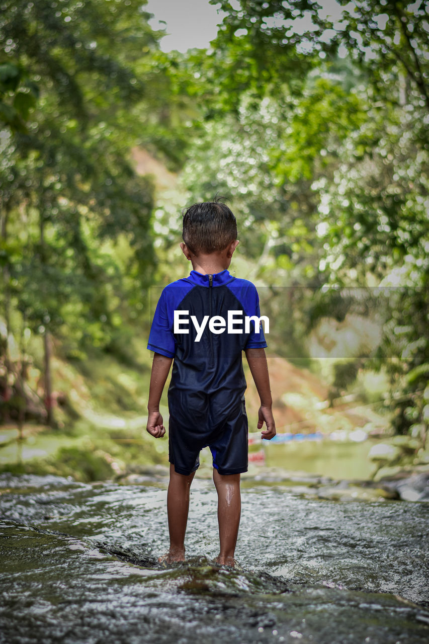 Rear view of boy standing in stream