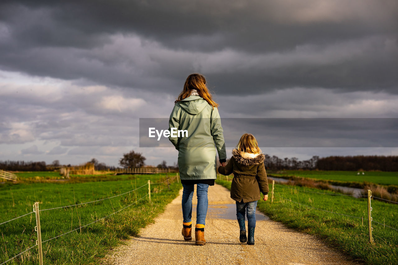 Rear view of mother and daughter walking on road against sky