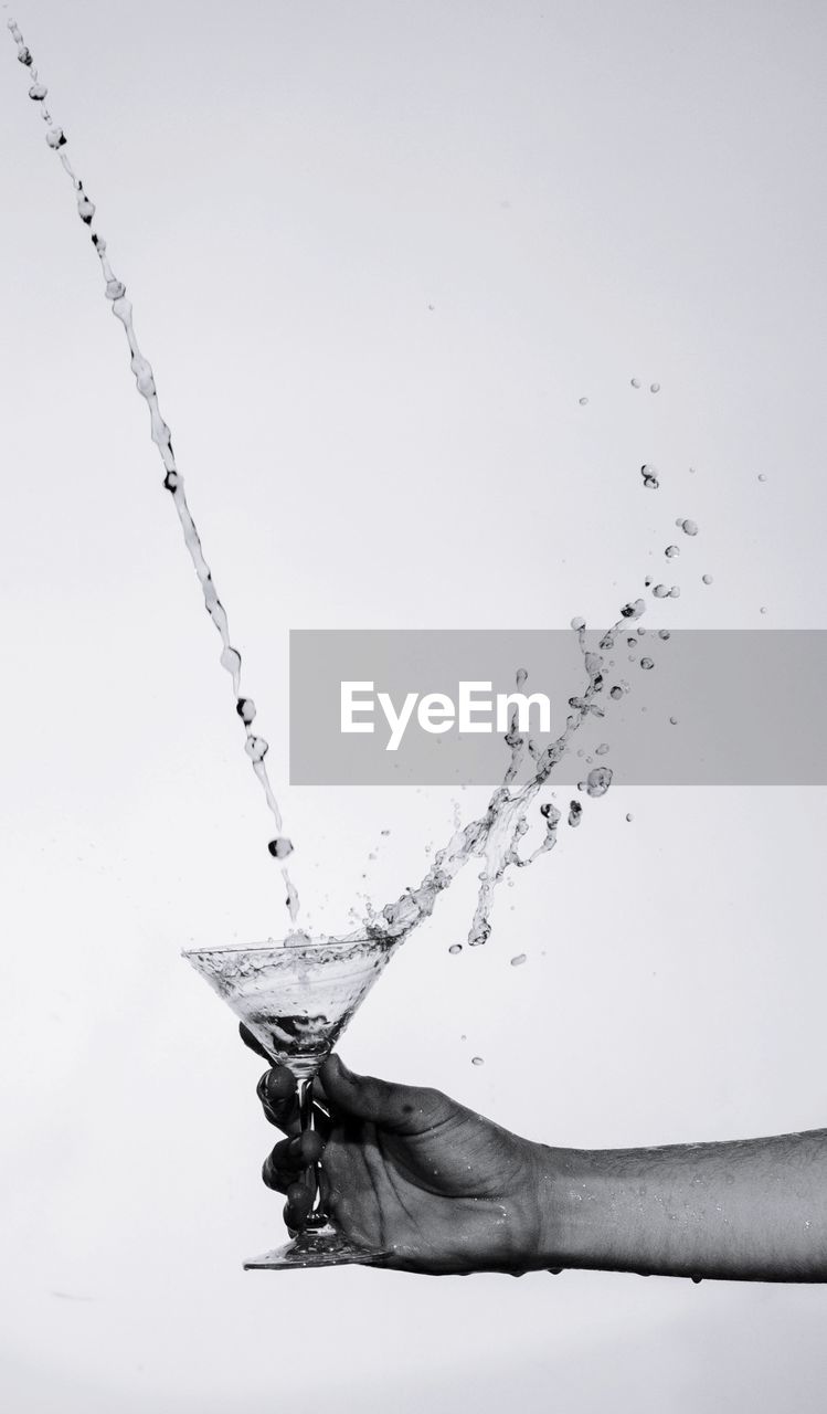 Cropped hand holding drink glass against white background