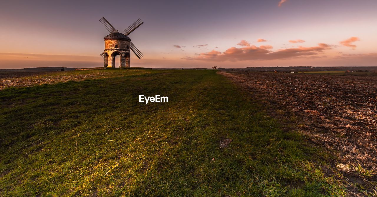 WINDMILLS ON FIELD AGAINST SKY DURING SUNSET