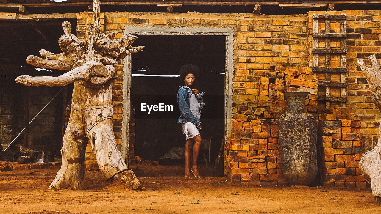 Portrait of young woman standing at doorway of abandoned building