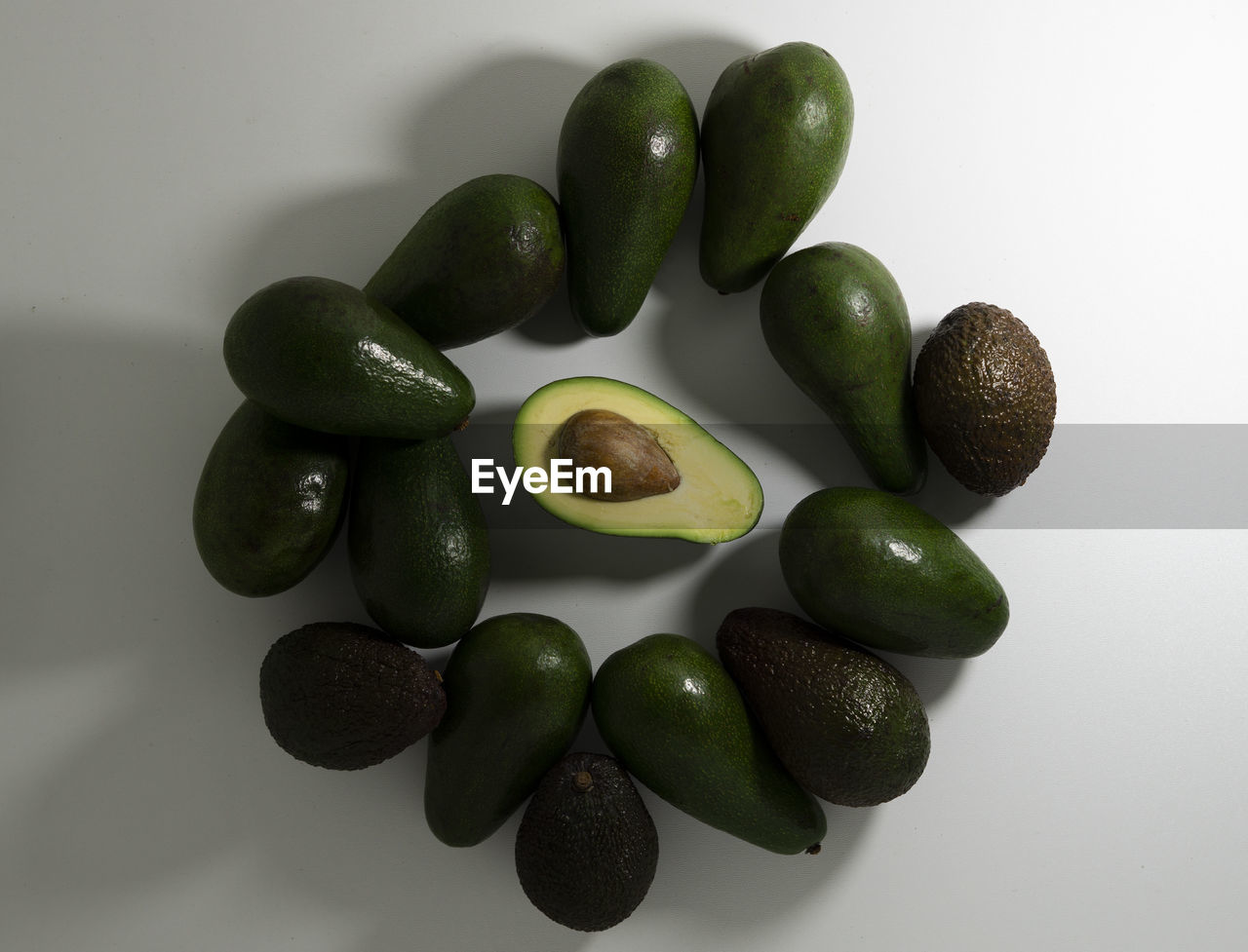 Sliced and whole avocado fruits of different varieties of green and brown on a light background.