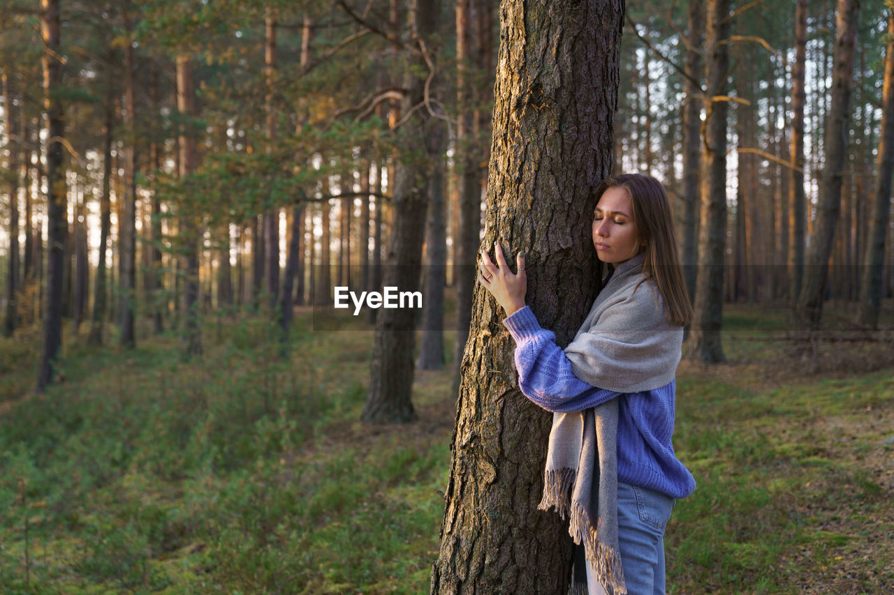 Unity with nature. young calm girl hugging pine tree trunk with closed eyes walking in autumn forest