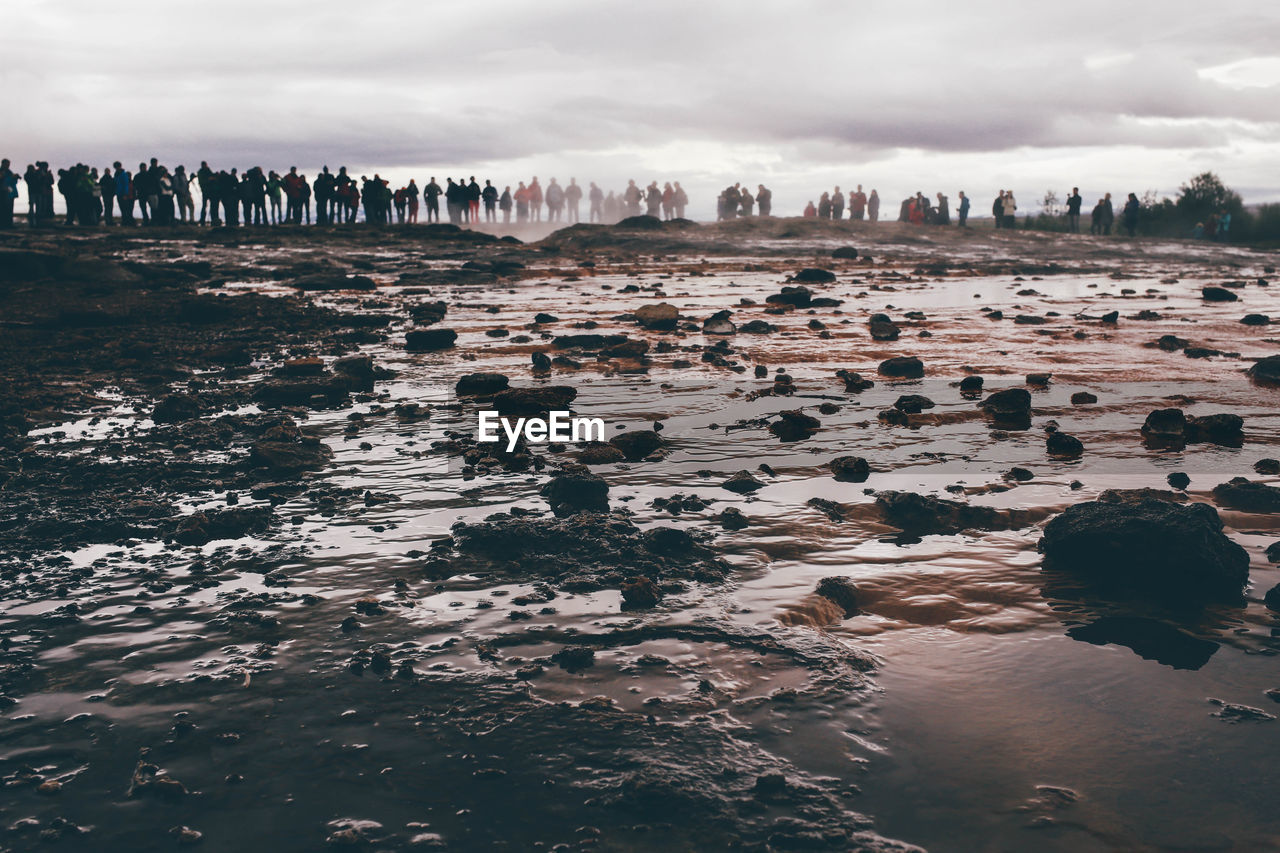 Distant view of people at geyser against sky