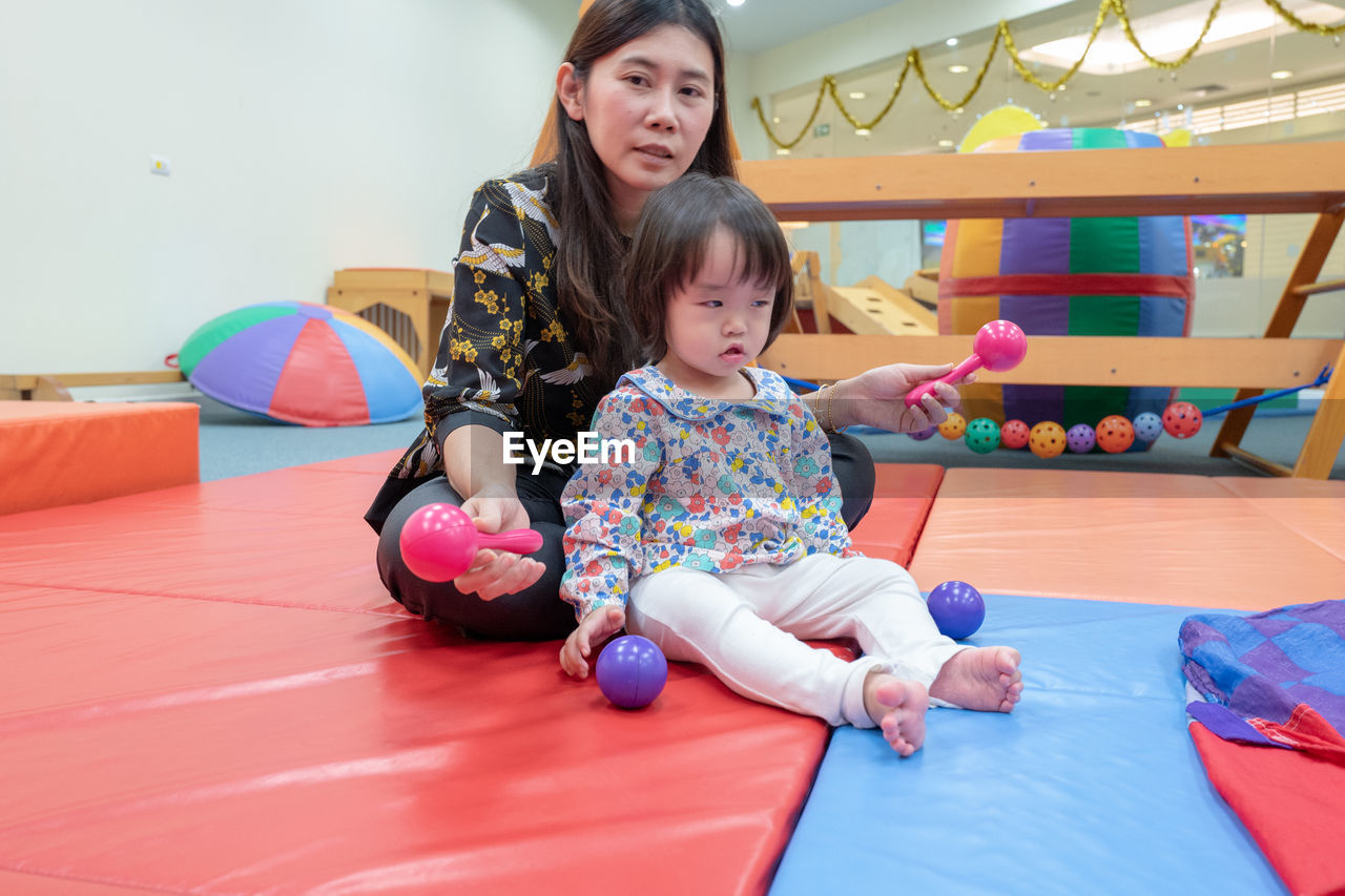 Cute girl with teacher playing on carpet in kindergarten