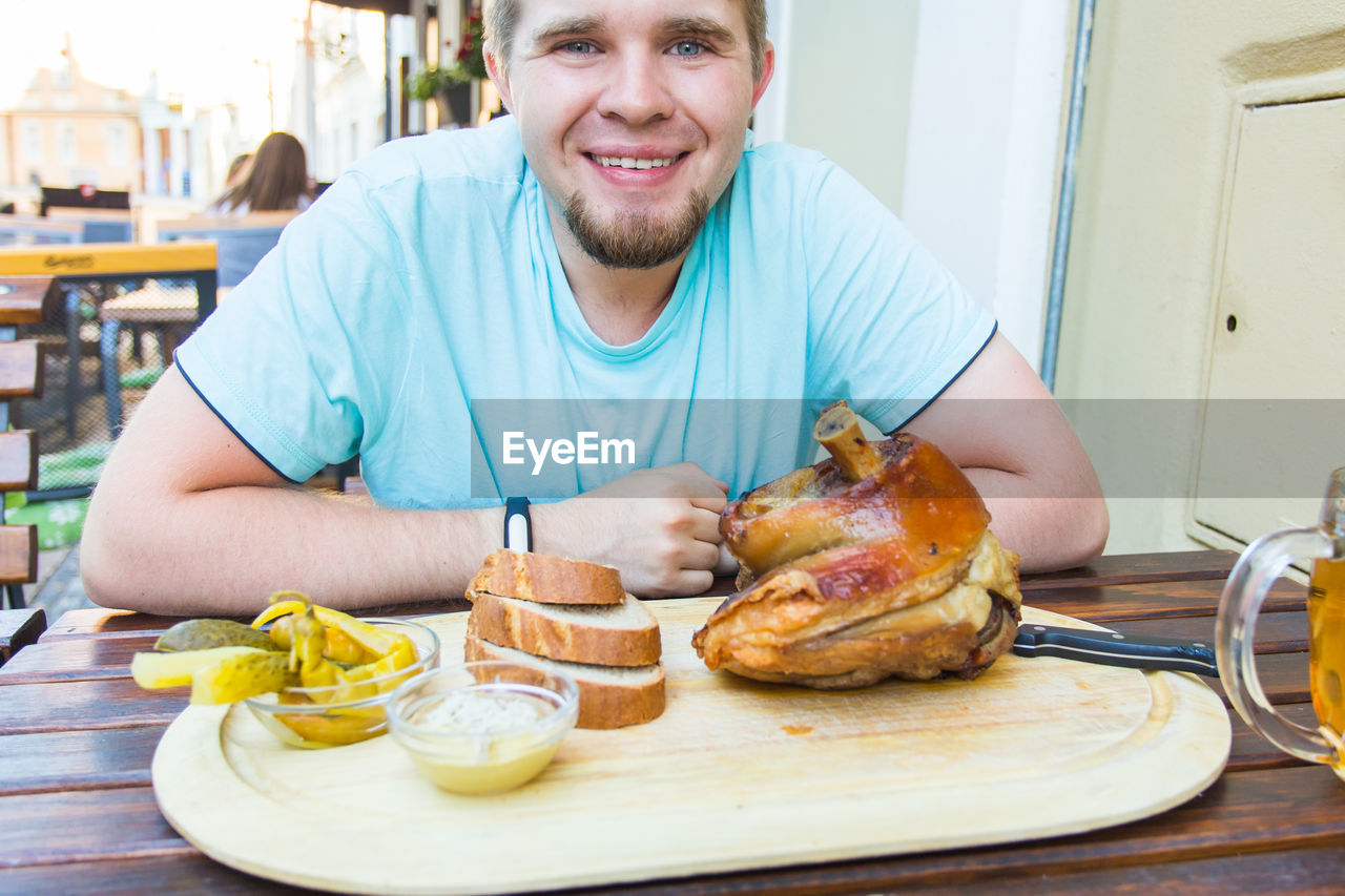 PORTRAIT OF HAPPY MAN SITTING WITH FOOD