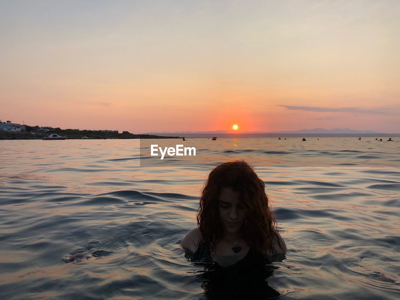 PORTRAIT OF YOUNG WOMAN AGAINST SEA DURING SUNSET