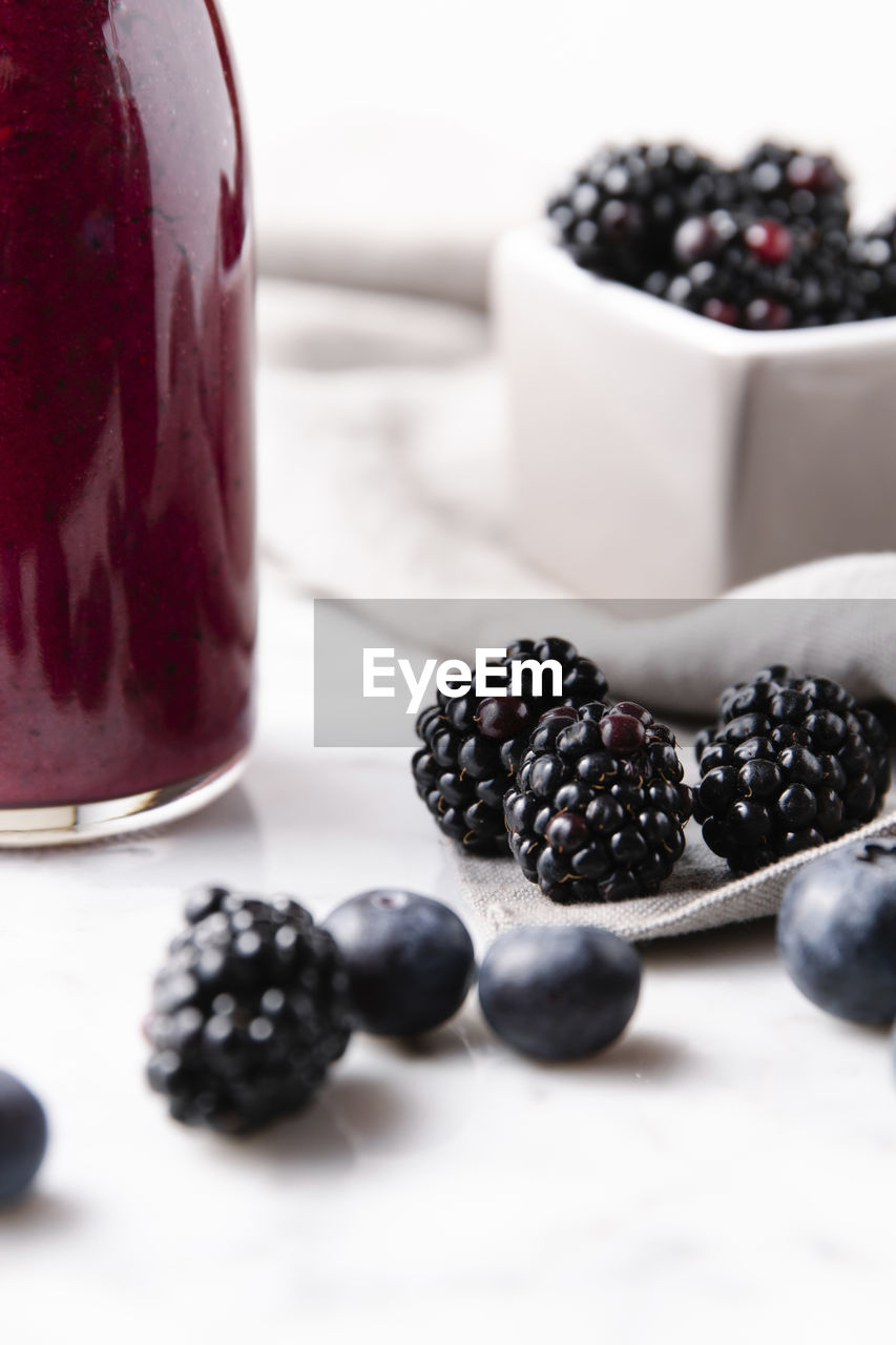Close up of blackberries beside blueberries and a glass bottle of smoothie on a marble surface. vertical image.