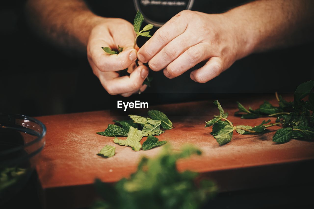 Cropped image of man plucking mint leaves over cutting board at counter