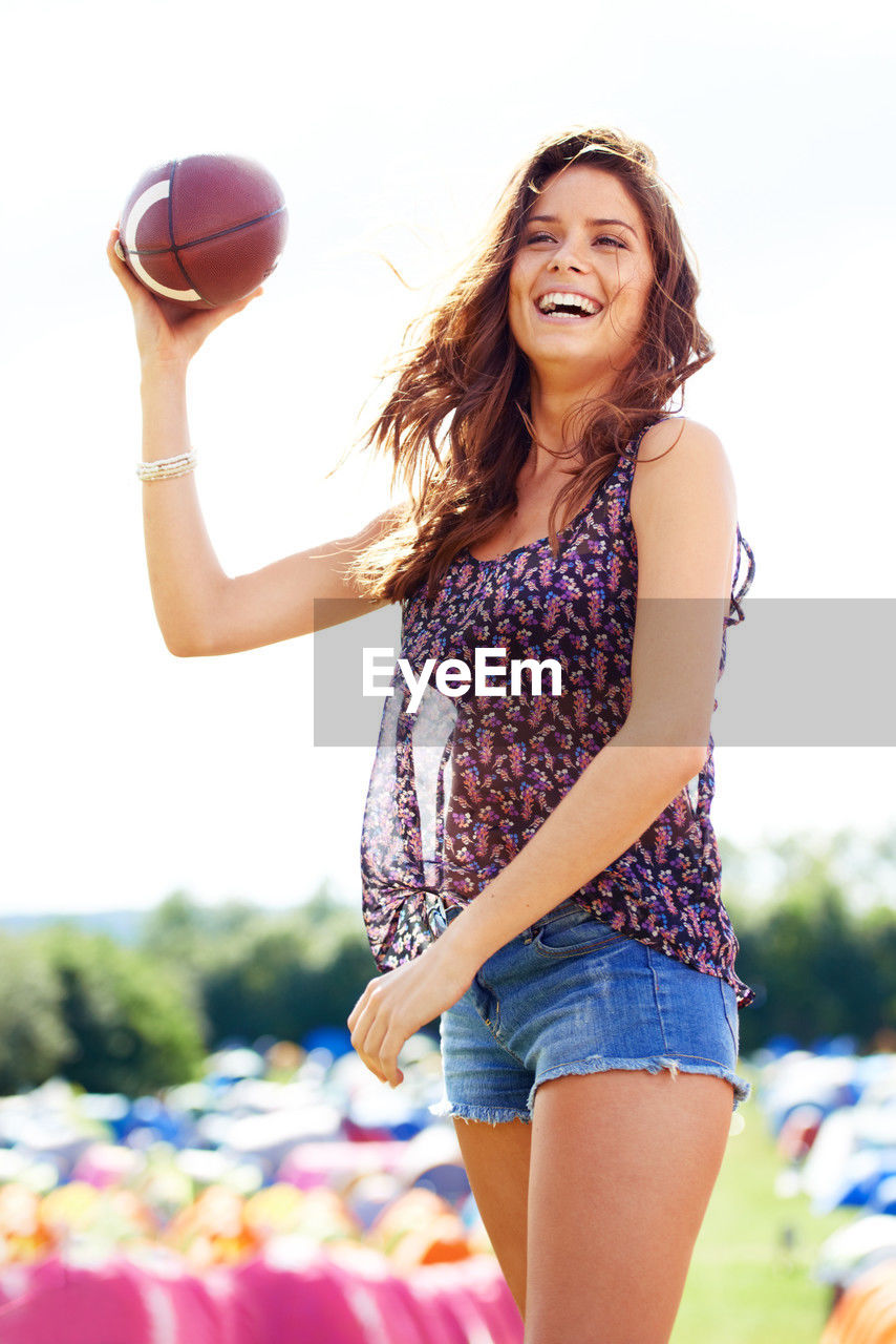 happiness, women, young adult, adult, smiling, one person, emotion, fun, shorts, long hair, leisure activity, enjoyment, summer, hairstyle, cheerful, carefree, casual clothing, lifestyles, nature, sports, brown hair, vitality, ball, relaxation, clothing, sunlight, day, motion, portrait, standing, teenager, three quarter length, positive emotion, laughing, person, joy, holding, outdoors, teeth, sky, smile, looking, limb, human limb, human face, recreation, fashion, photo shoot, weekend activities