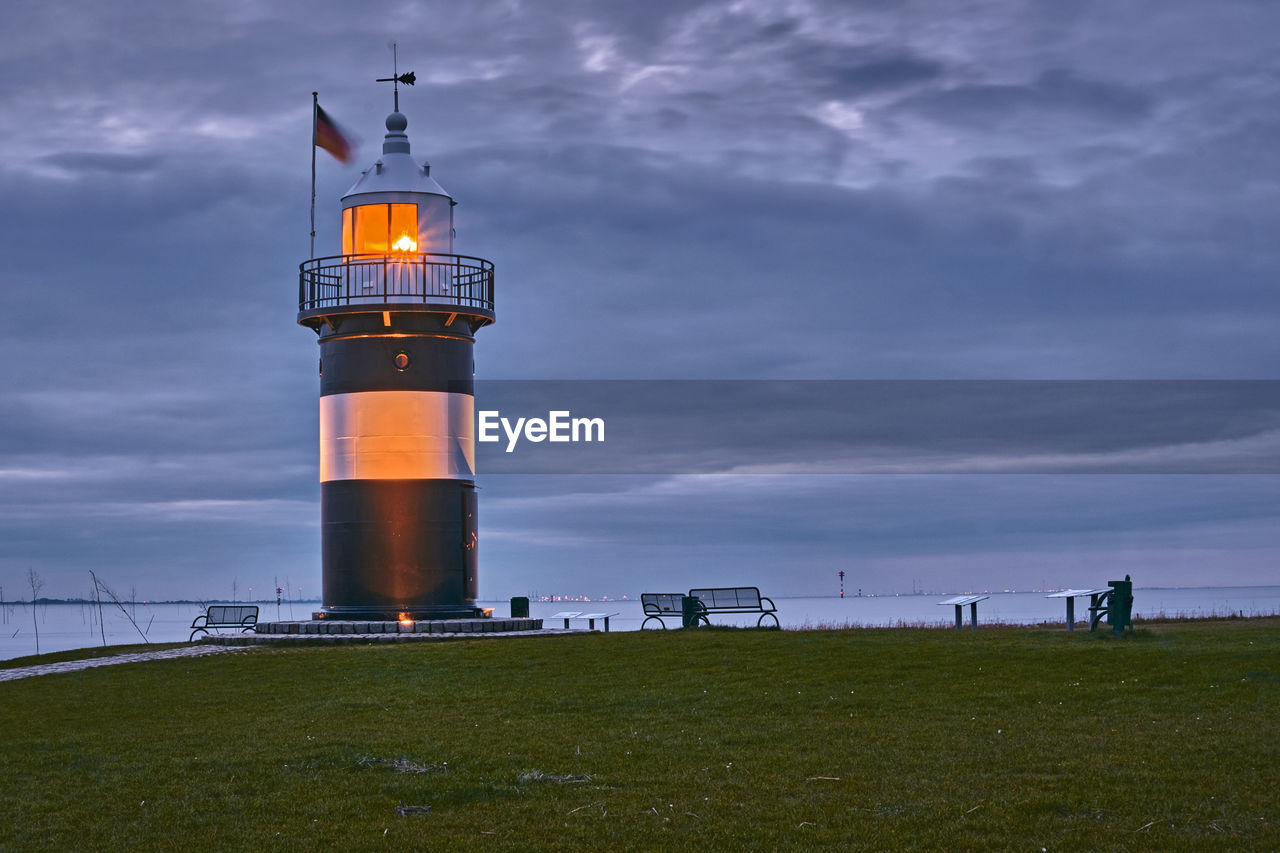 Lighthouse on field by building against sky